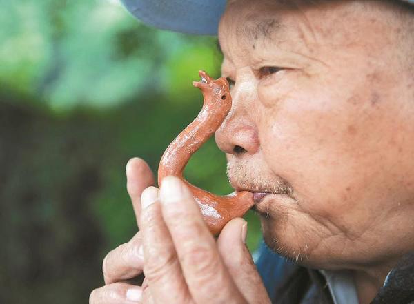 萬富冊老人為過往市民吹奏泥鵝子。