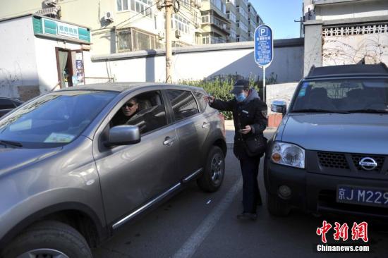 今年元月起，北京全市3000多名路側停車管理員上崗證更換，新上崗證標有二維碼，市民用手機掃描即可看到管理員的照片、姓名、所在公司、監(jiān)督電話等詳細信息。若冒用或偽造，掃描出來的信息將與實際不符，一旦遇到假收費員，市民有權拒絕交費。圖為停車場管理員張大姐為車主指揮倒車。<a target='_blank' href='http://www.chinanews.com/' >中新網</a>記者 金碩 攝