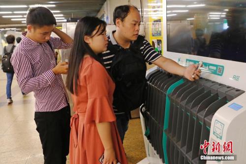 圖為沒(méi)帶雨傘的民眾在共享雨傘的貨架上掃碼借用。殷立勤 攝