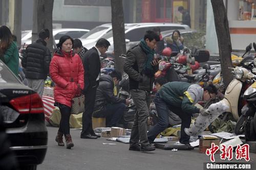 一家快遞公司的員工蹲在馬路邊分發(fā)郵件，身邊堆放著大量的包裹。 王中舉 攝 